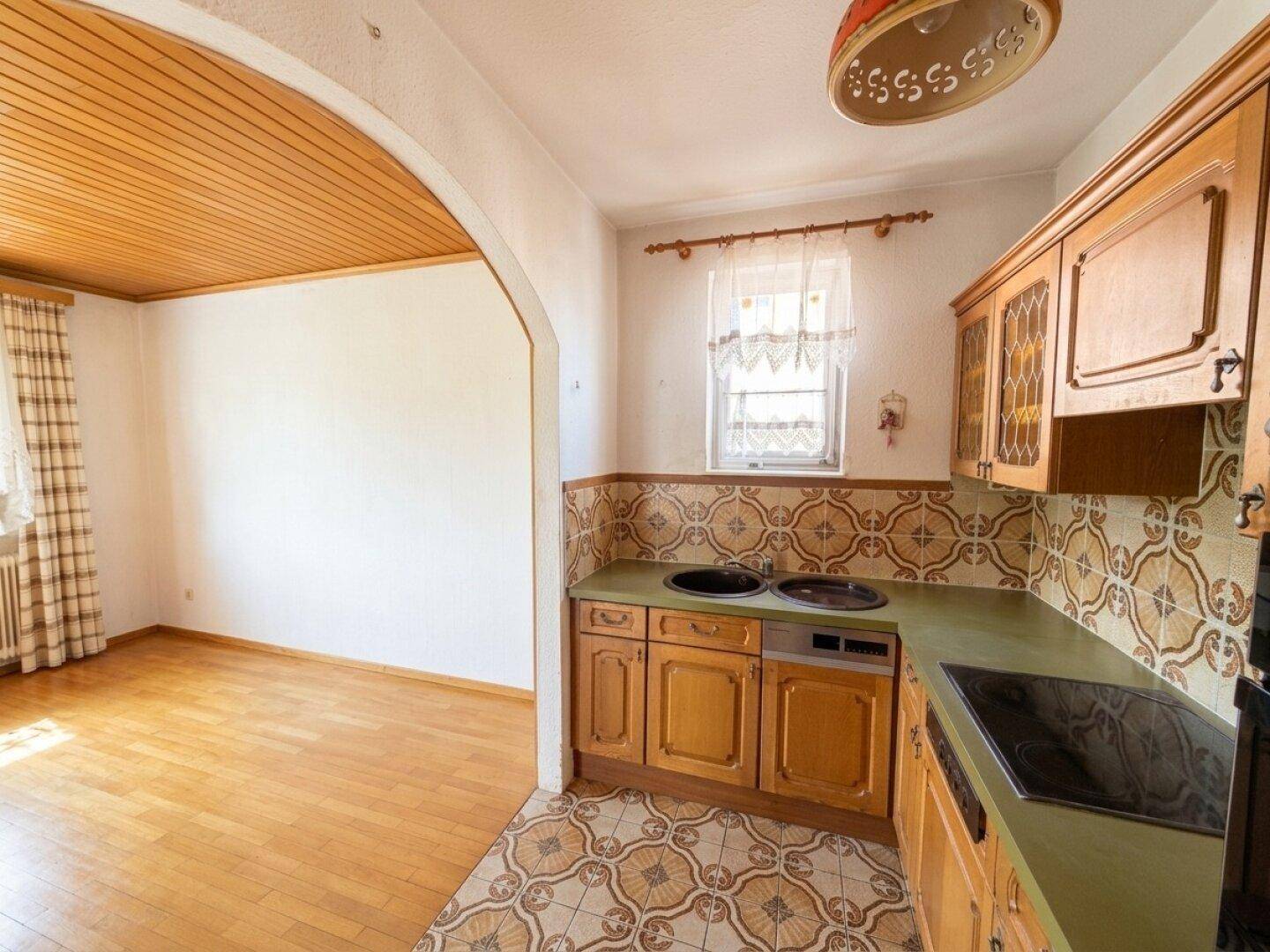 Küche mit traditionellen Holzschränken und gemusterten Fliesen, offen zum angrenzenden Raum.