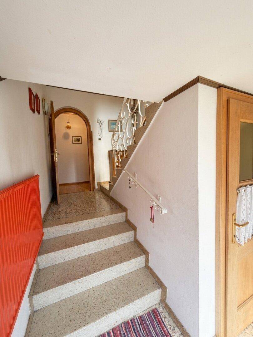 Treppenhaus mit Steinstufen, rotem Heizkörper und Zugang zu weiteren Räumen.