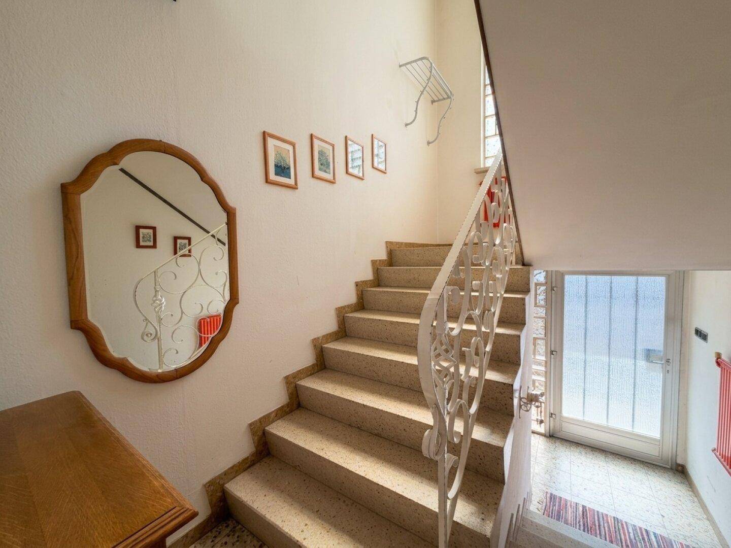 Treppenhaus mit Steinstufen, Spiegel und Bildern an der Wand.