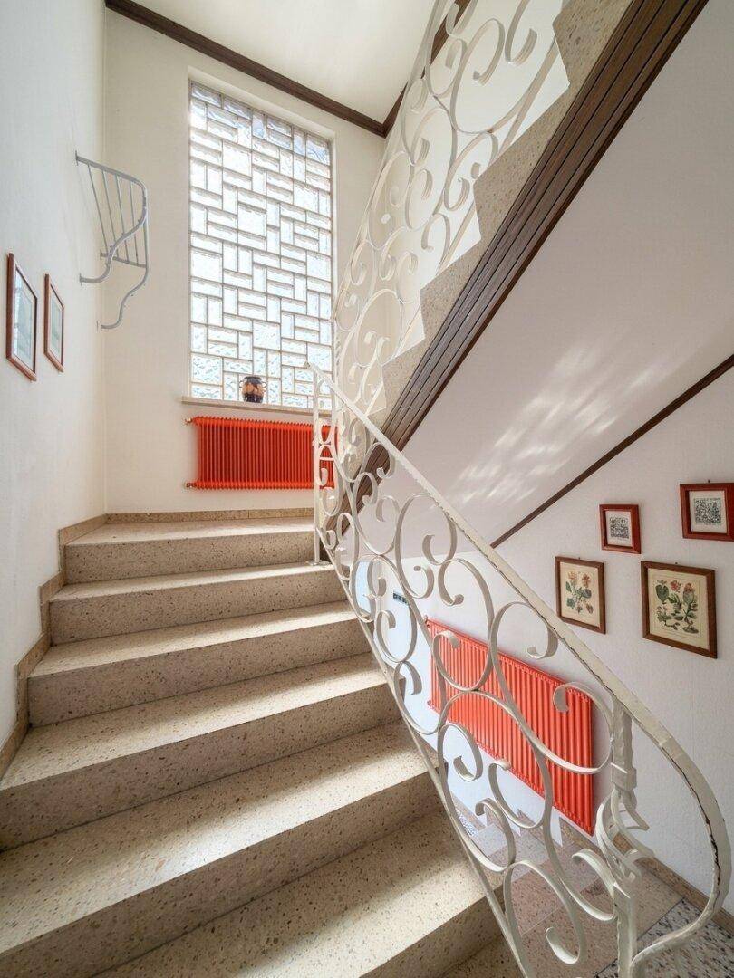 Treppenhaus mit Steinstufen, rotem Heizkörper und Glasbausteinfenster.