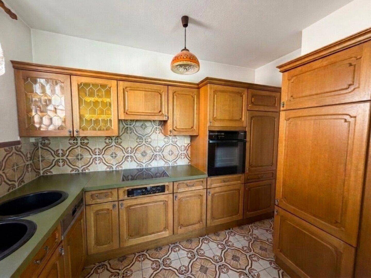 Gut erhaltene Holzküche mit gemusterten Fliesen, integriertem Backofen und Kochfeld.