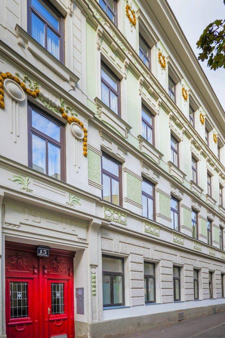 Historische Fassade eines Altbaus mit kunstvollen Verzierungen und markanten roten Eingangstüren.