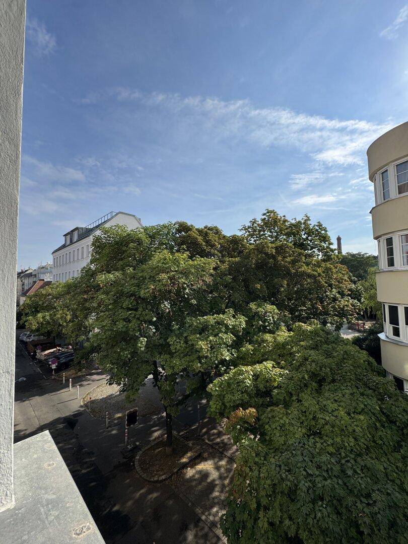 Weitblick von einem Balkon über eine von Bäumen gesäumte Straße und die Stadt.