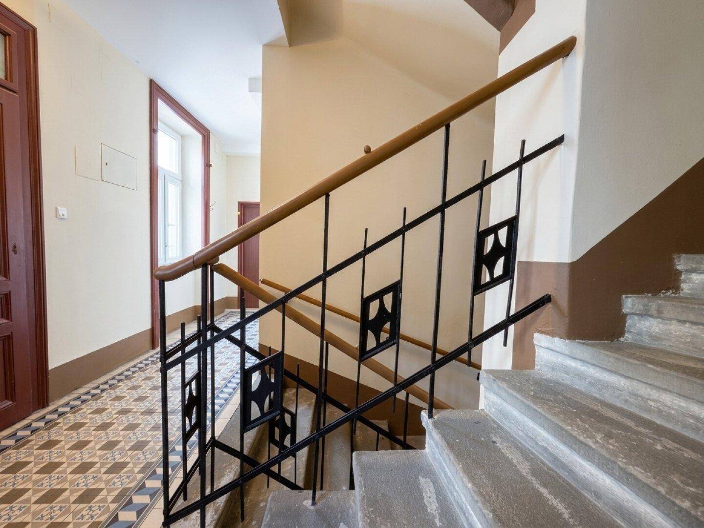 Detailansicht des schmiedeeisernen Treppengeländers mit Holzhandlauf in einem Altbau.