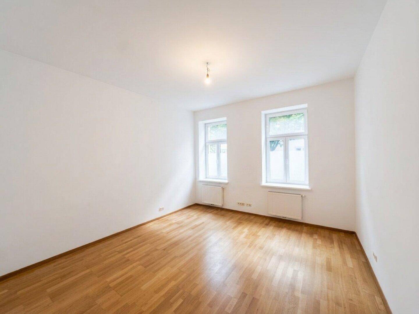 Leerer Raum mit Parkettboden und zwei Fenstern, bereit zur individuellen Gestaltung.