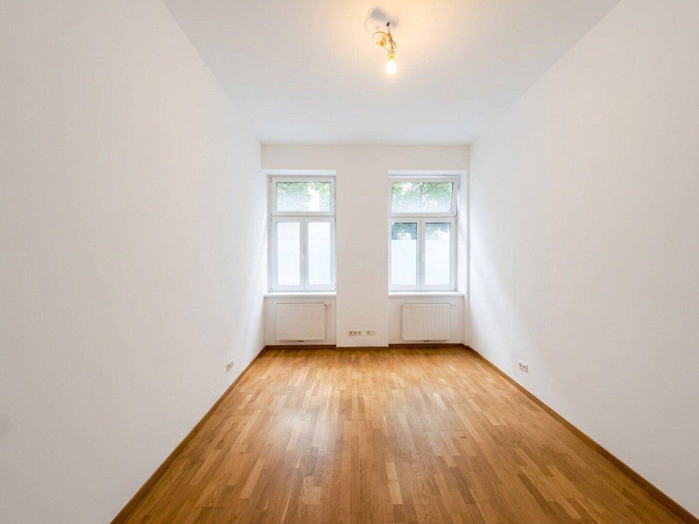 Unmöblierter Raum mit Parkettboden und zwei Fenstern, bietet vielseitige Einrichtungsmöglichkeiten.