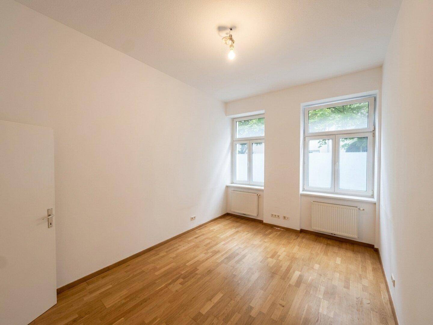Leerer Raum mit Holzboden und Fenstern, ideal für Schlafzimmer oder Arbeitszimmer.