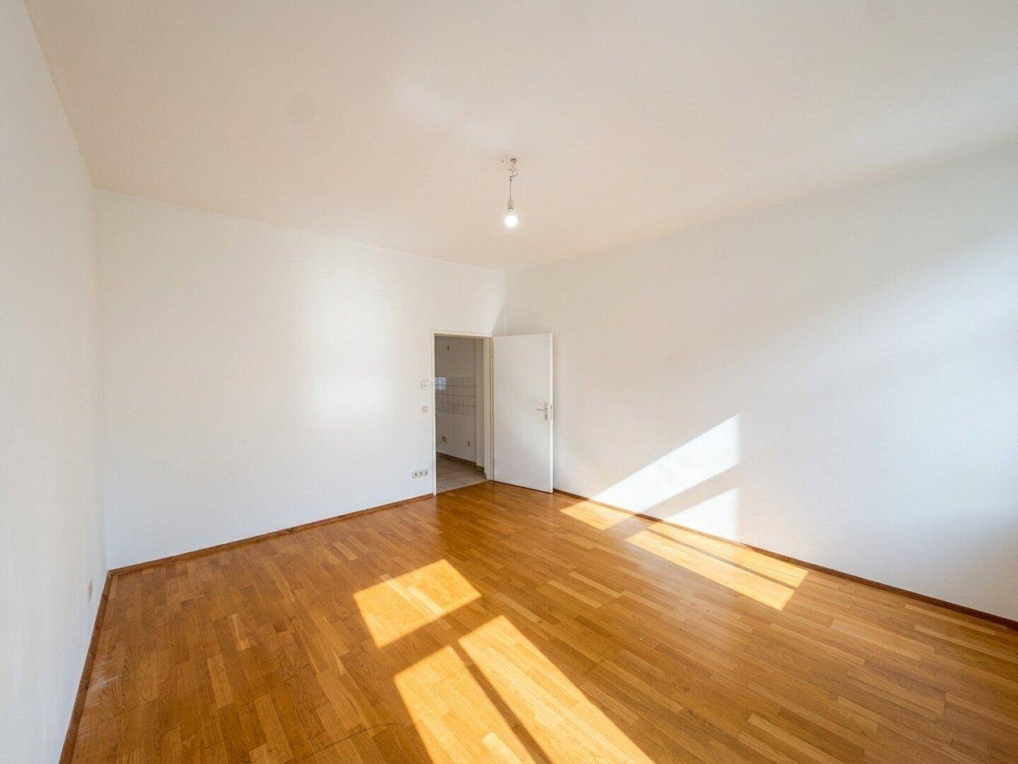 Geräumiges, leeres Zimmer mit Parkettboden und viel natürlichem Lichteinfall, ideal für Schlafzimmer.