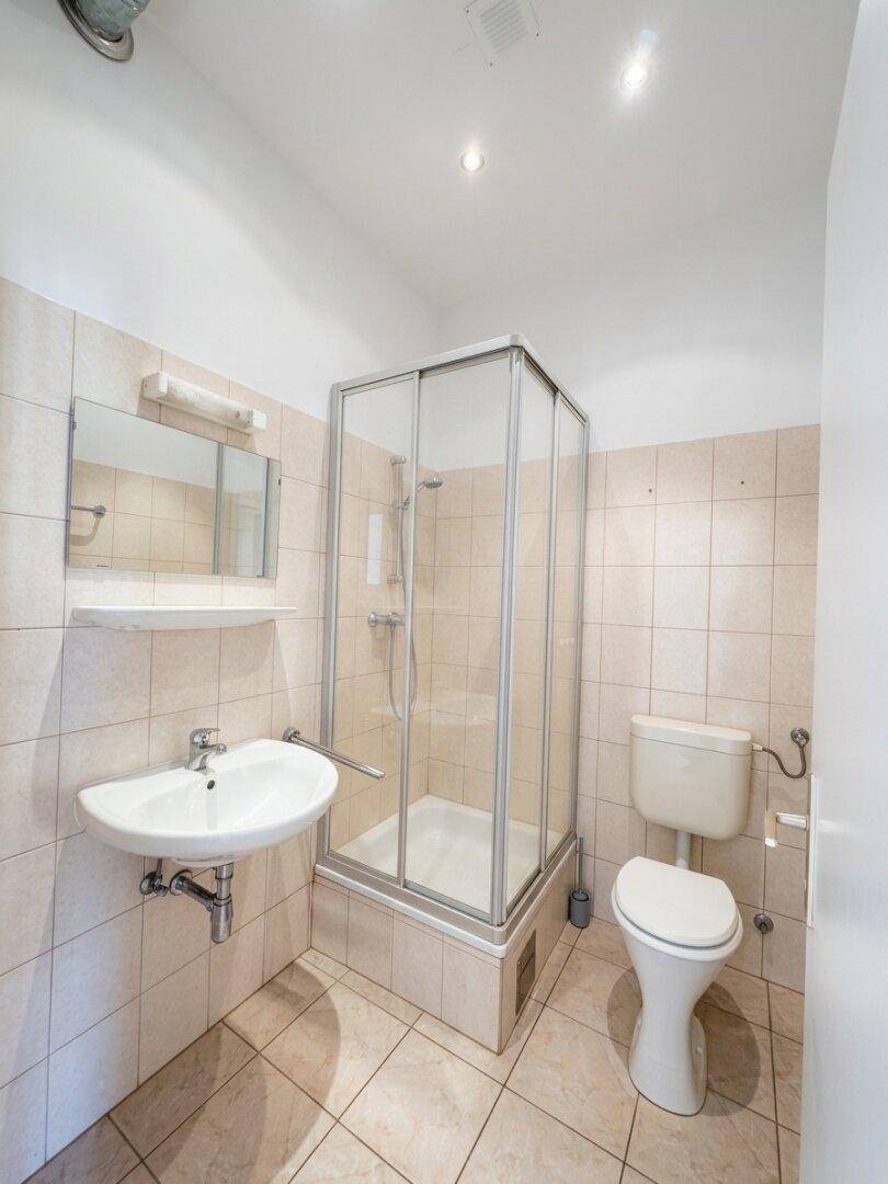 Funktionales Badezimmer mit Dusche, WC und Waschbecken, hell gefliest und gut erhalten.
