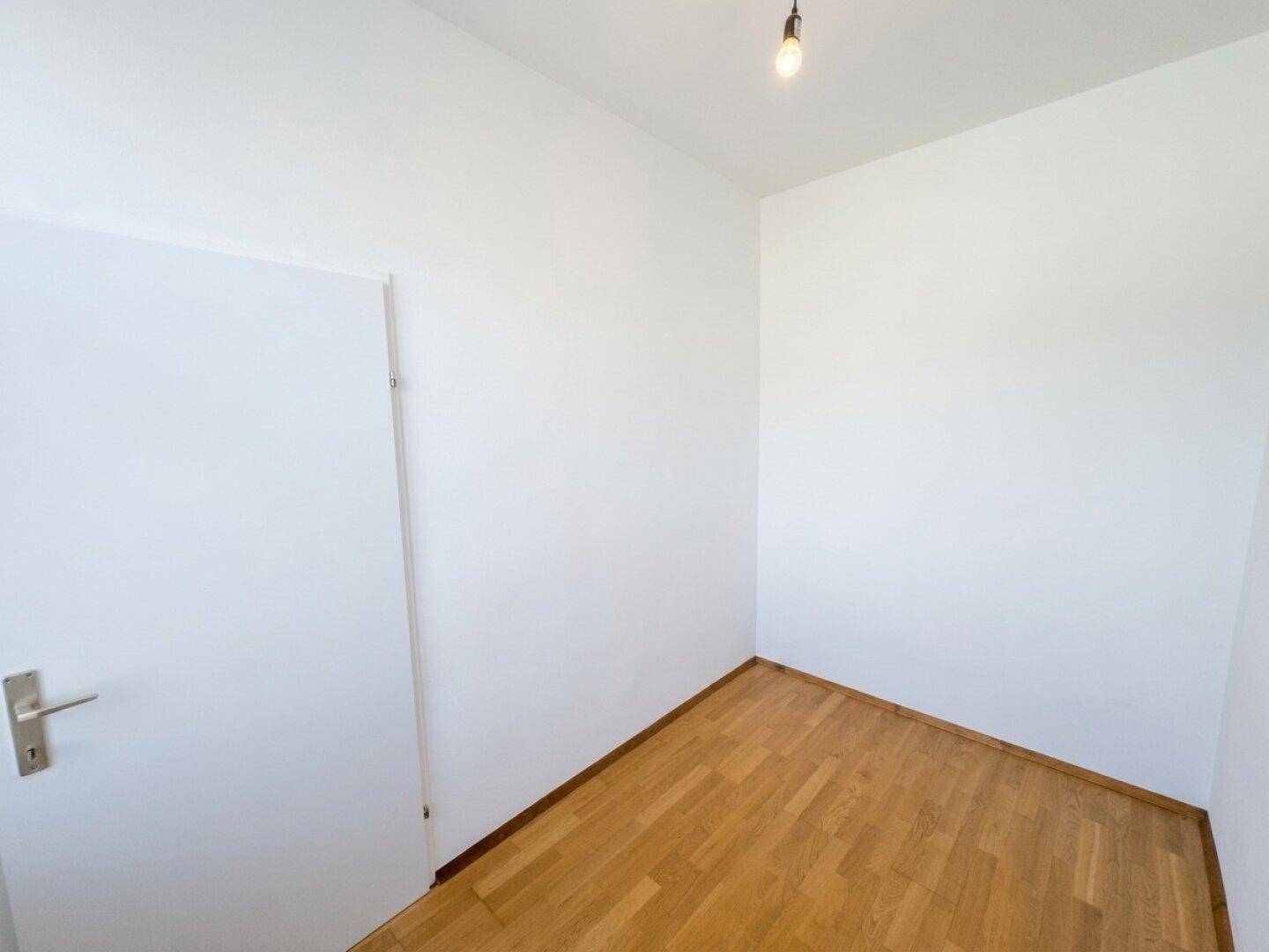 Leeres Zimmer mit Parkettboden und weißer Tür, bereit für individuelle Einrichtungsideen.