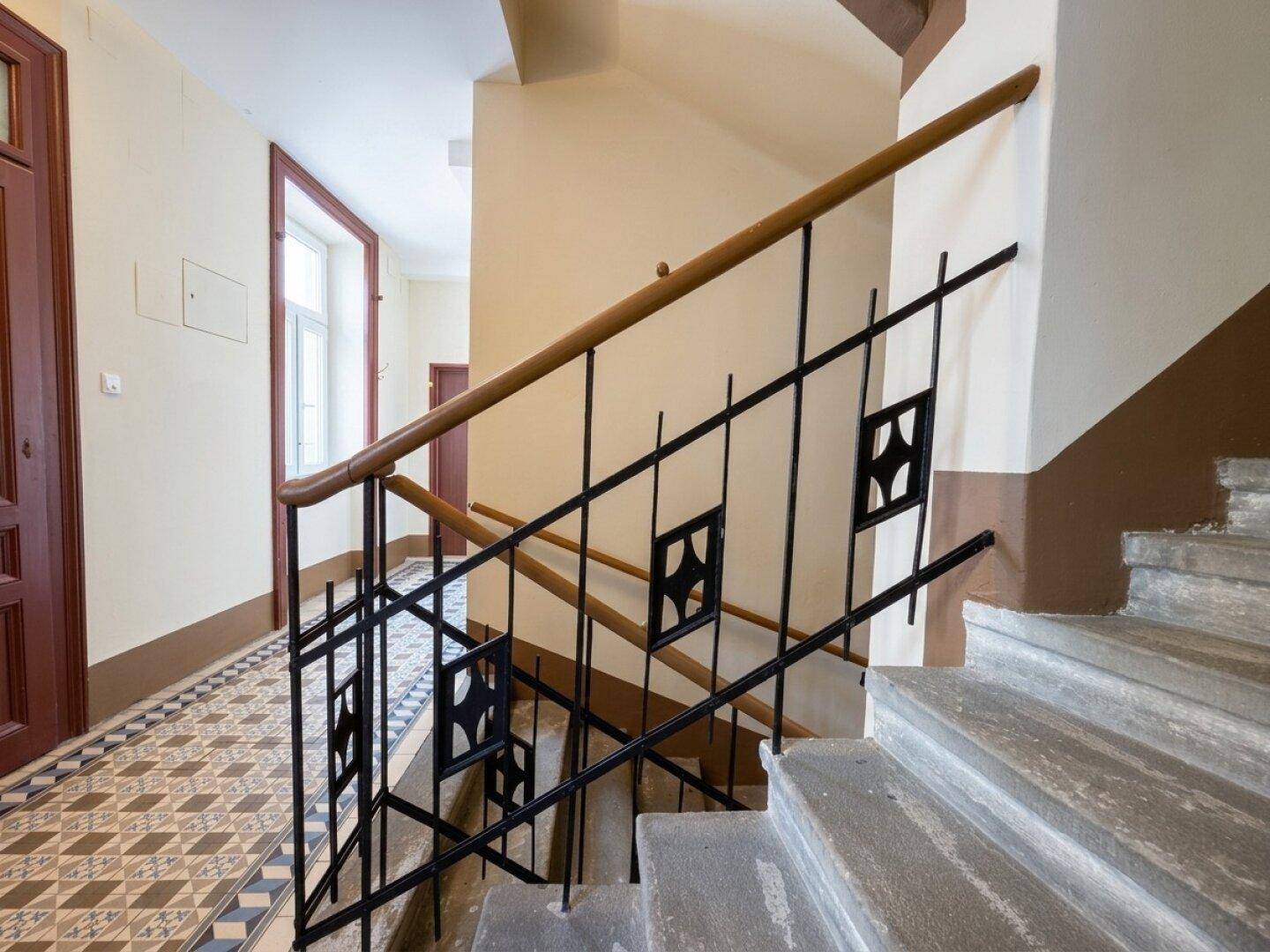 Treppenhaus mit Holzhandlauf und schmiedeeisernem Geländer, typisch für einen Altbau.