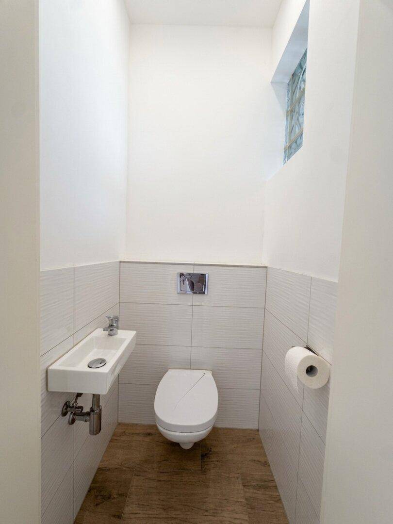 Modernes Gäste-WC mit wandhängender Toilette, kleinem Waschbecken und Holzoptik-Fliesenboden.