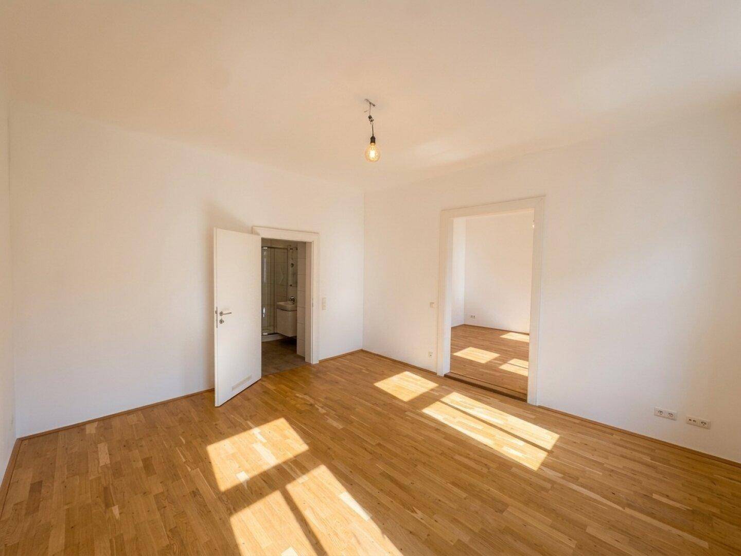 Heller, unmöblierter Raum mit Parkettboden und Zugang zu weiteren Zimmern, ideal für ein Wohnzimmer.