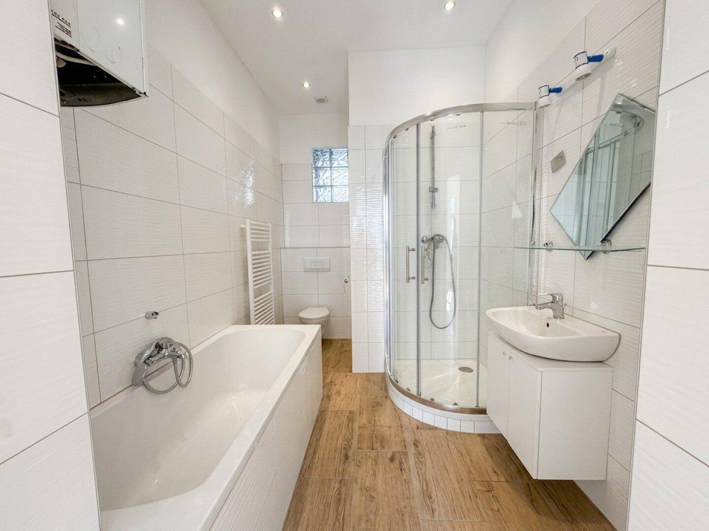 Modernes Badezimmer mit Badewanne, Duschkabine und Holzoptik-Fliesenboden.