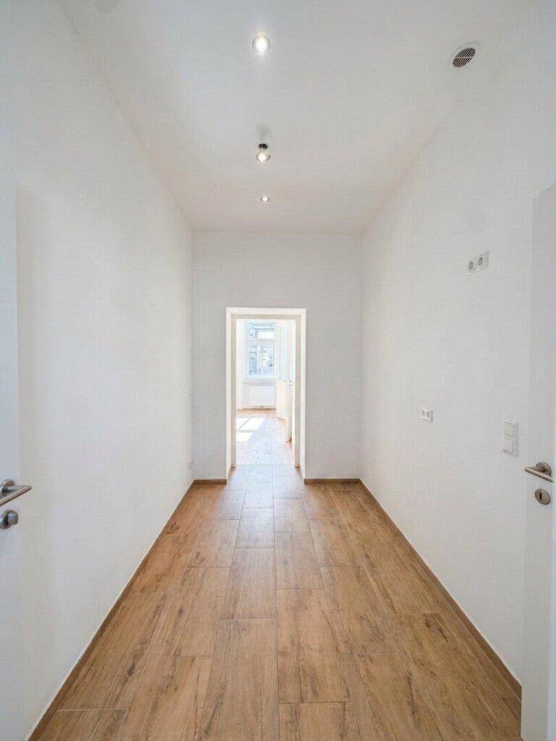 Heller Flur mit Holzoptik-Fliesenboden und Einbaustrahlern, der zu einem weiteren Raum führt.