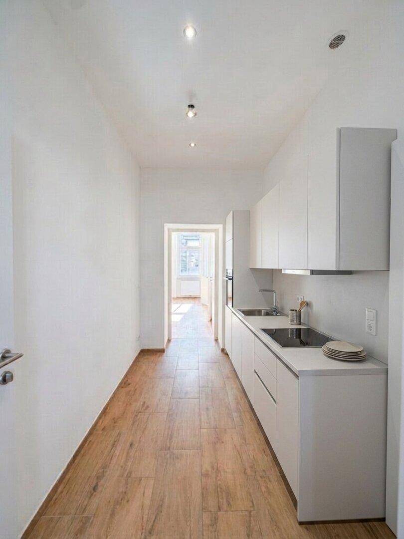Schmale, moderne Küche mit weißen Schränken, integrierten Geräten und Holzoptik-Fliesenboden.