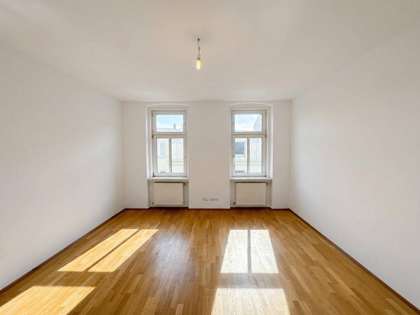 Helles, unmöbliertes Zimmer mit Holzboden und zwei Fenstern, ideal für vielfältige Nutzung.