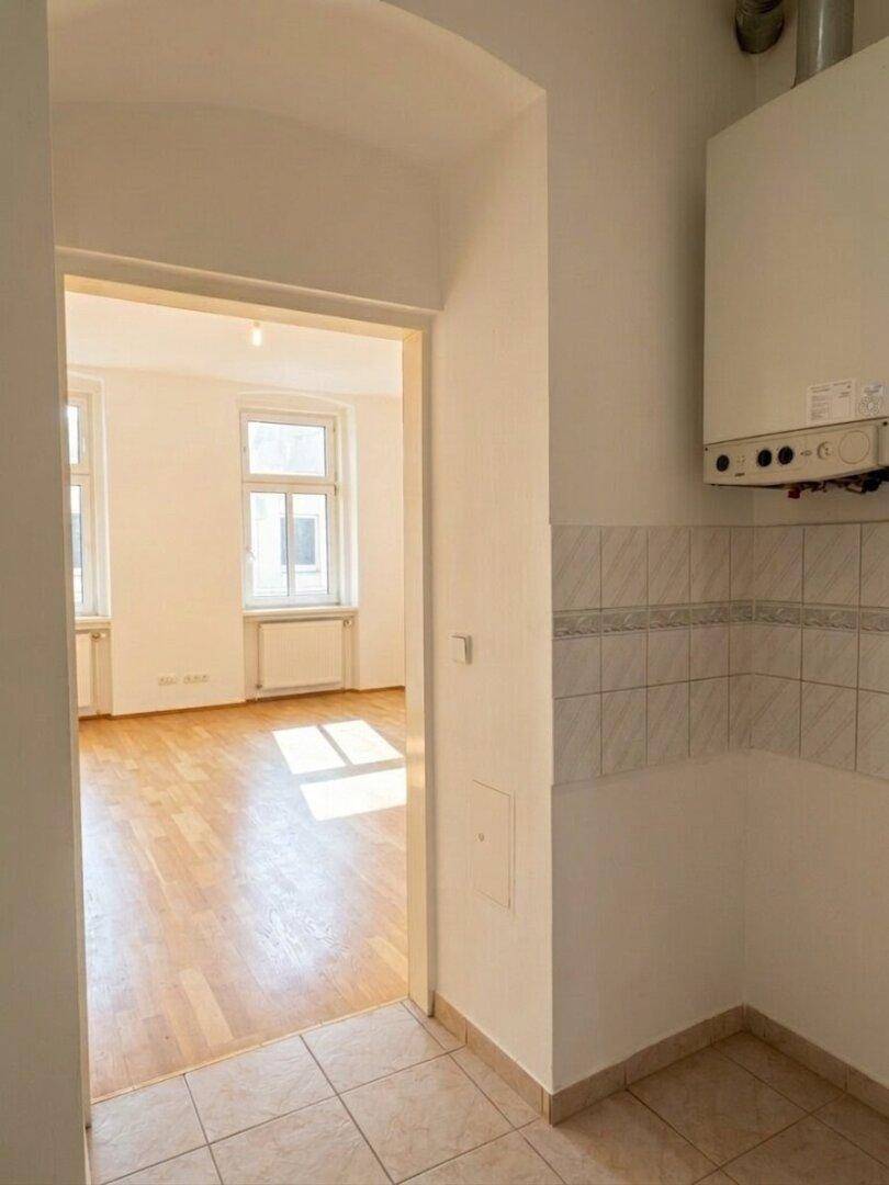 Bereich mit Fliesenboden und Wandfliesen, vorbereitet für eine Küche, mit Blick in ein weiteres Zimmer.