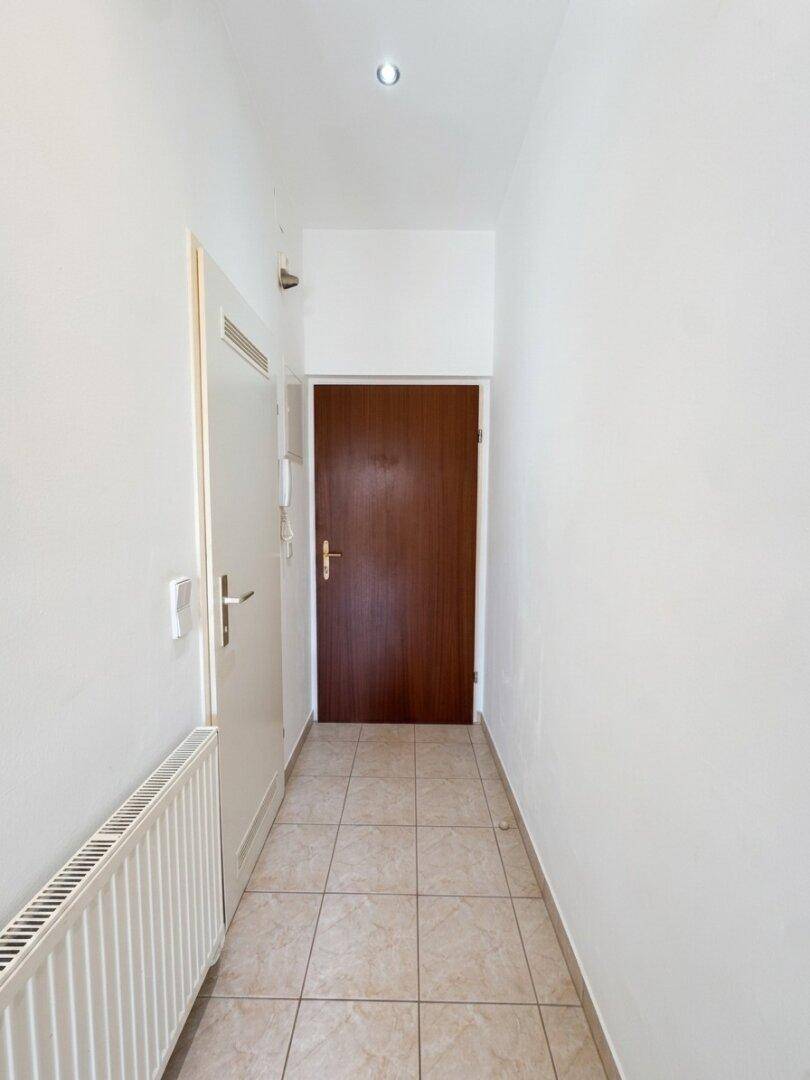 Heller Flur mit Fliesenboden und einer dunklen Eingangstür, ausgestattet mit einer Gegensprechanlage.