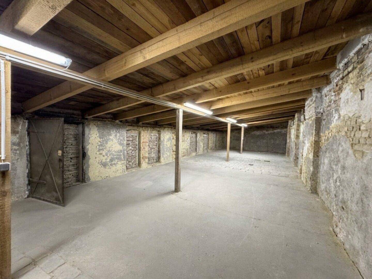 Geräumiger Kellerraum mit Holzbalkendecke, unverputzten Ziegelwänden und Betonboden.