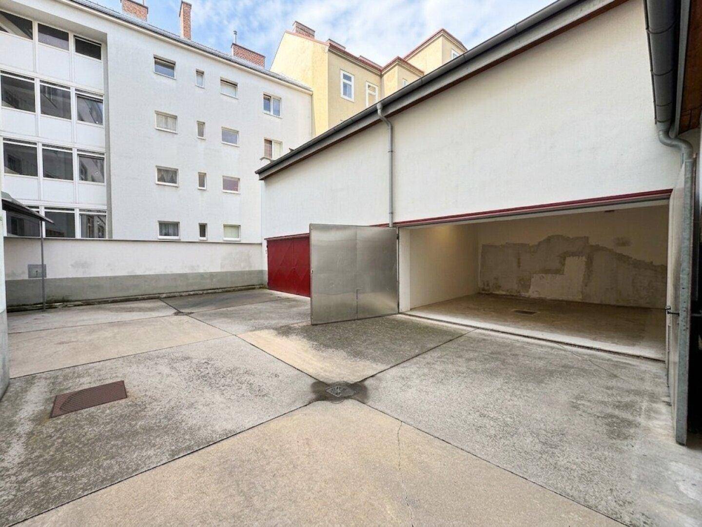 Offene Garage mit Blick auf den gepflasterten Innenhof und umliegende Gebäude.