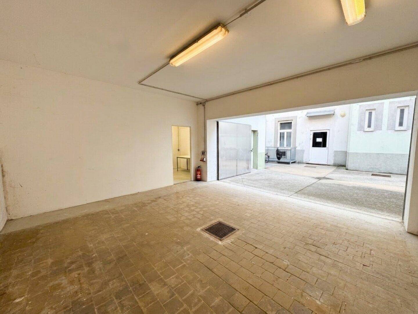 Innenansicht einer Garage mit Fliesenboden und Blick auf den hellen Innenhof.