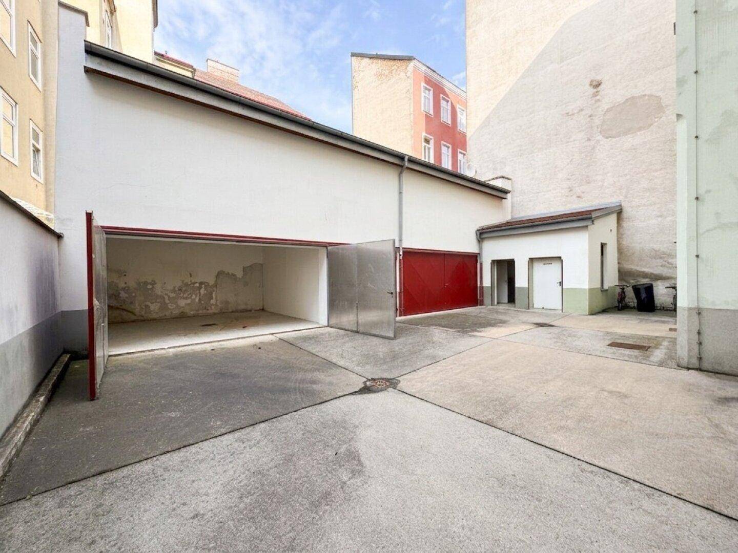 Offene Garage mit Metalltüren und einem kleinen Nebengebäude im Innenhof.