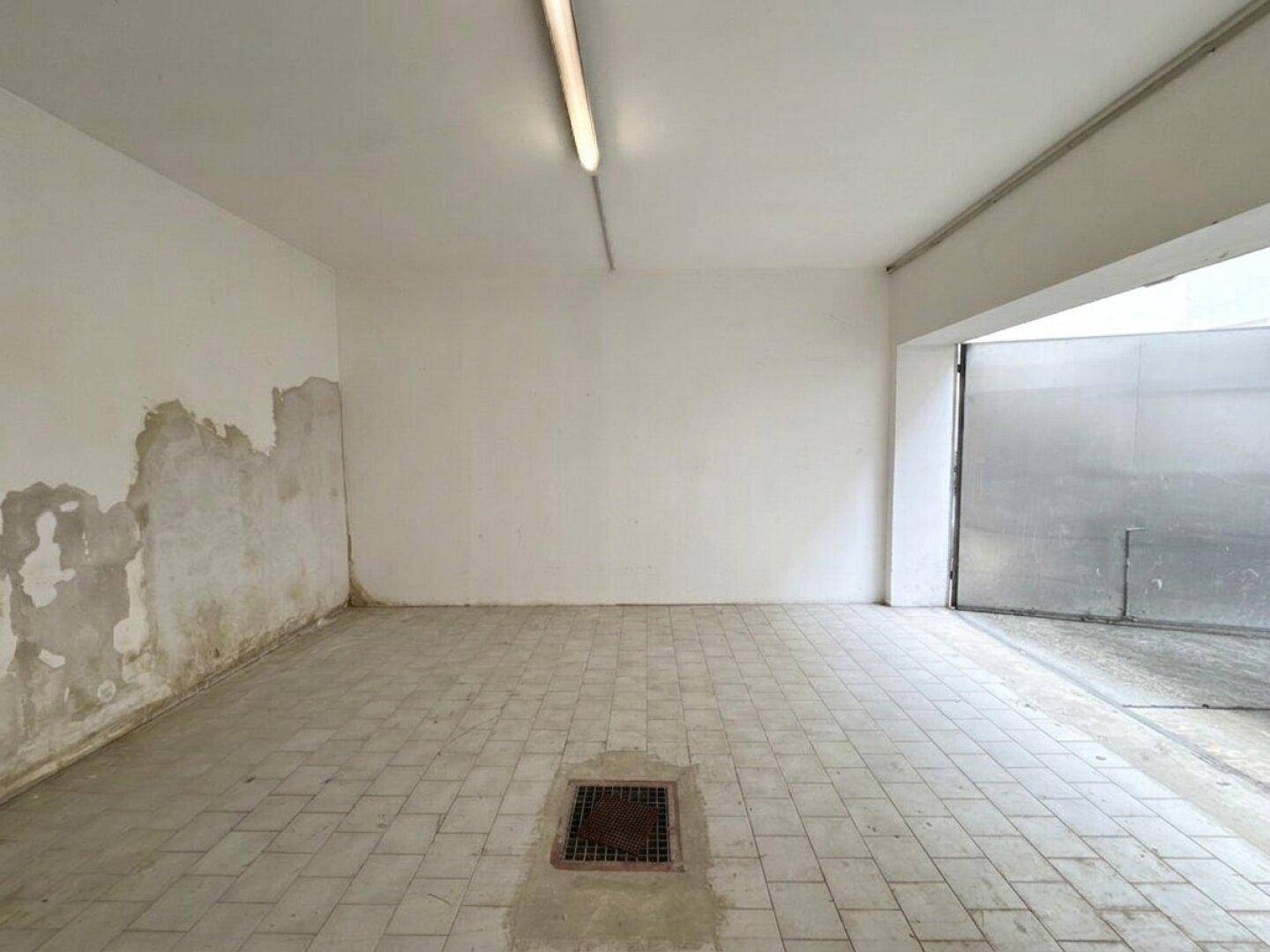 Geräumiger Garagenraum mit Fliesenboden und einer teilweise beschädigten Rückwand.