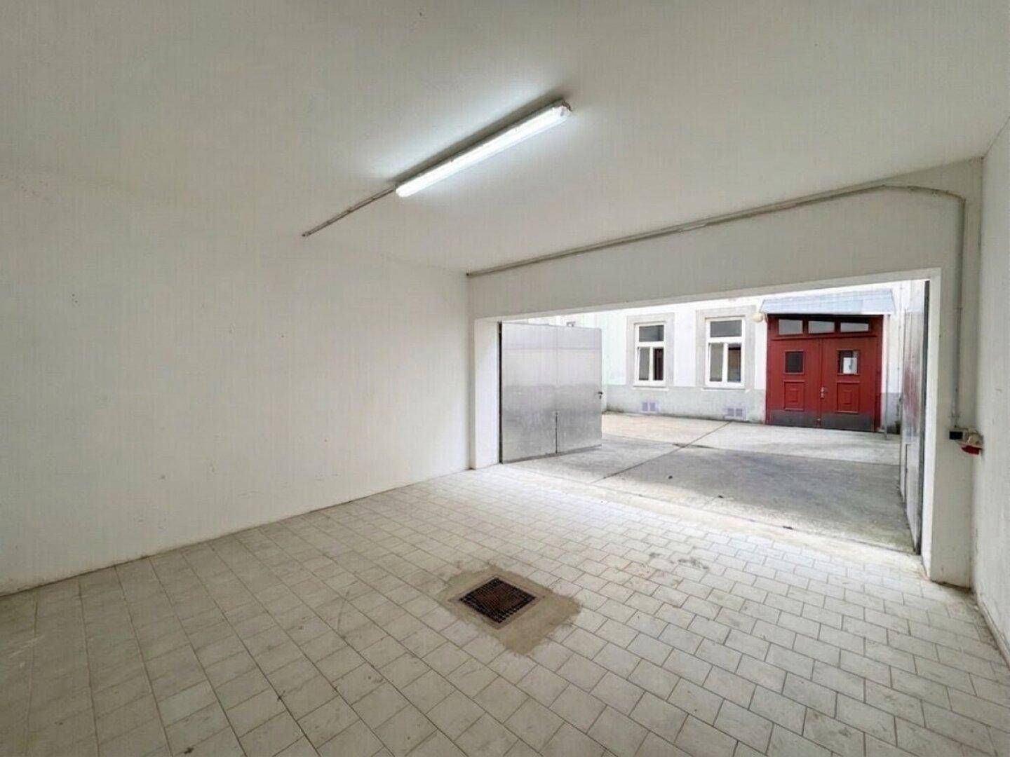 Innenansicht einer Garage mit hellen Fliesen und Blick auf den Außenbereich.