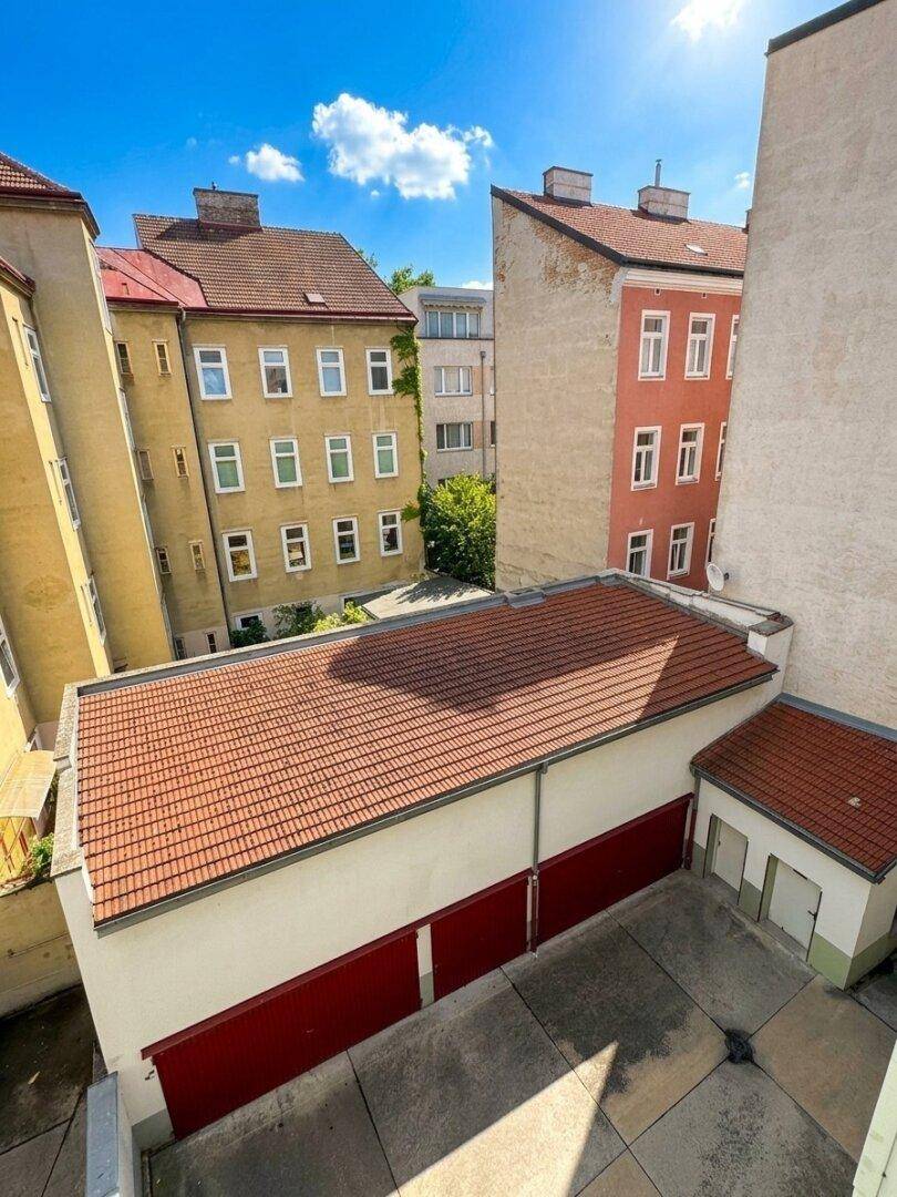 Panoramablick auf einen sonnigen Innenhof mit Garagen und angrenzenden historischen Wohngebäuden.