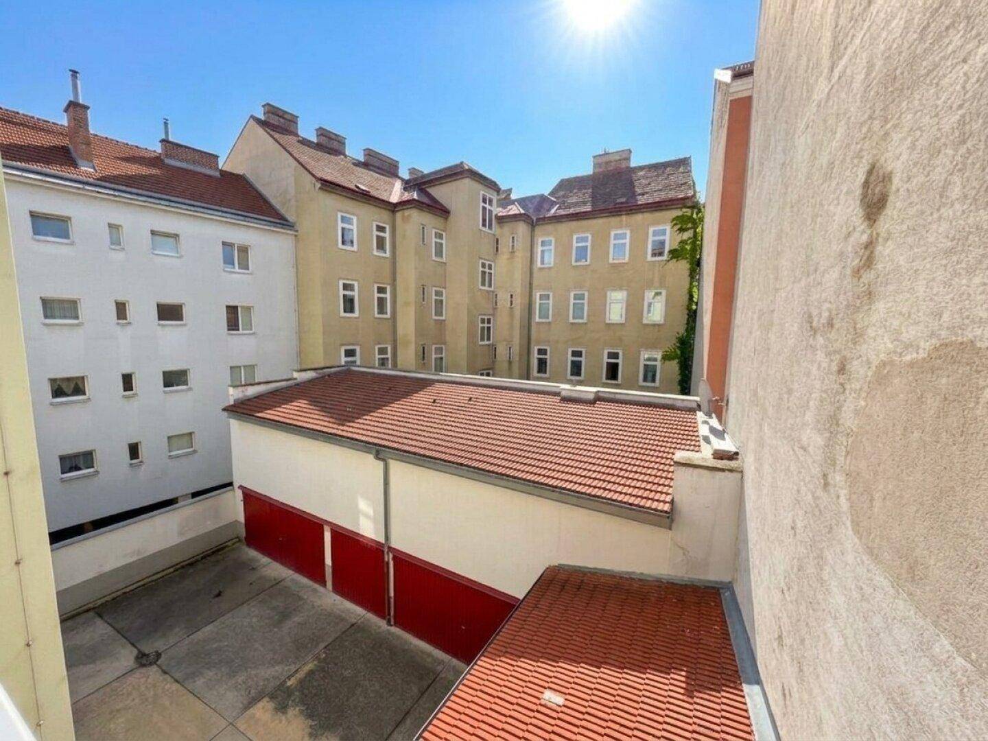Blick von oben auf einen Innenhof mit Garagen und umliegenden Wohngebäuden an einem sonnigen Tag.