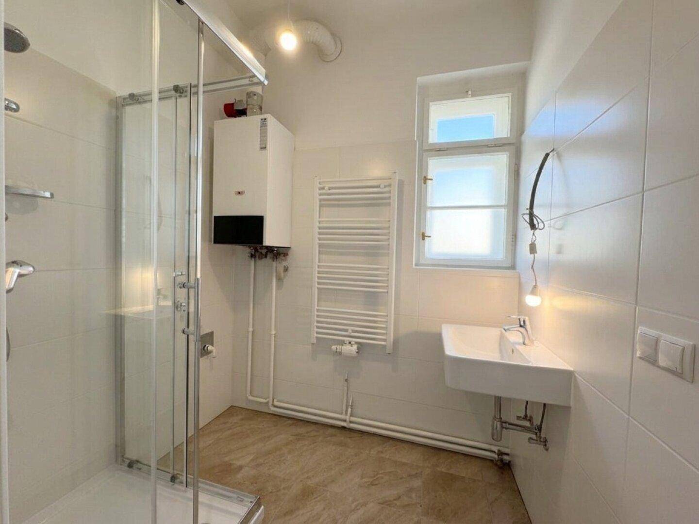 Modernes Badezimmer mit Dusche, Waschbecken, Handtuchheizkörper und Fenster für natürliche Belüftung.