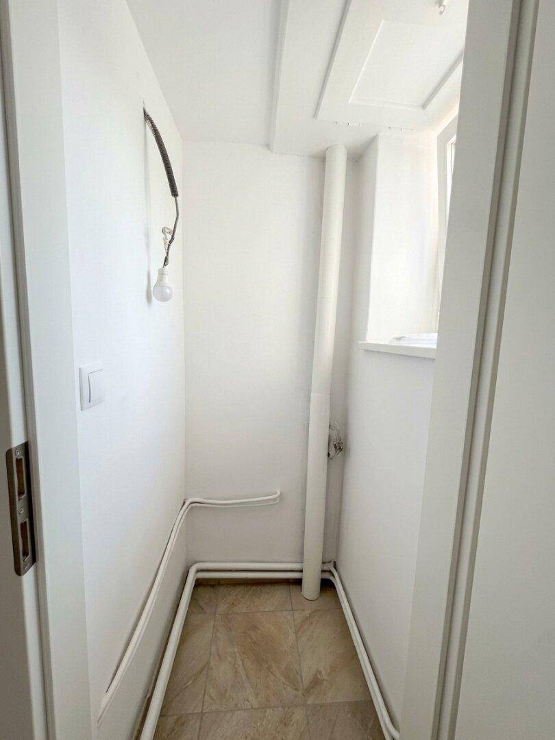 Kleiner Abstellraum mit Fliesenboden und sichtbaren Leitungen, ideal für Lagerung oder Technik.