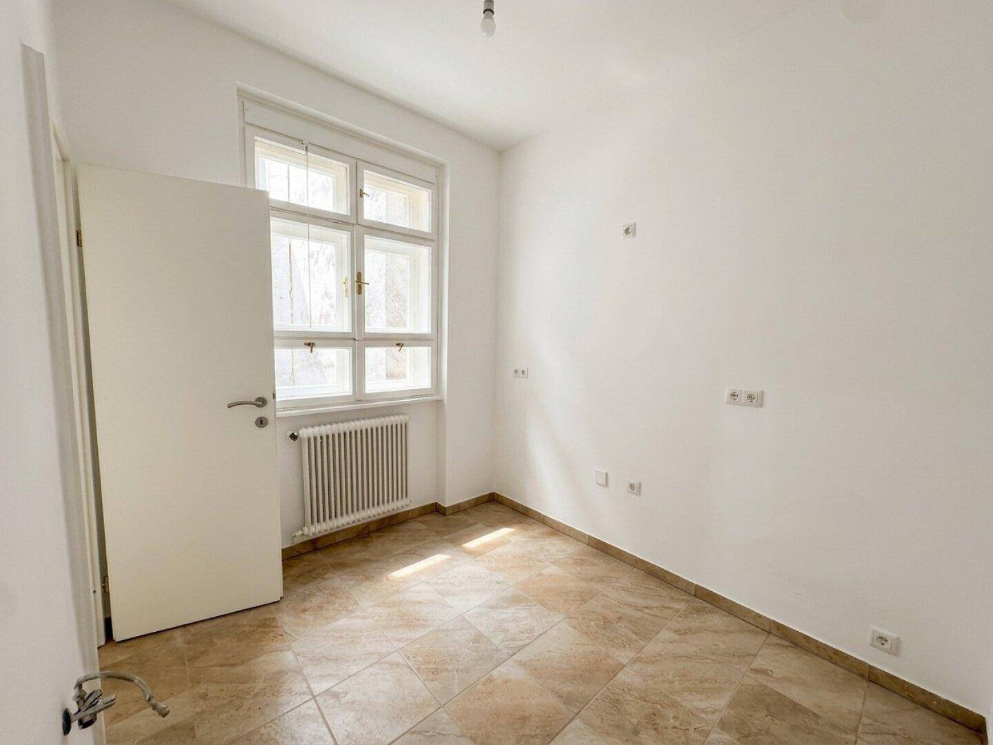 Kleiner Raum mit Fliesenboden und Fenster, vorbereitet für die Installation einer Küche.