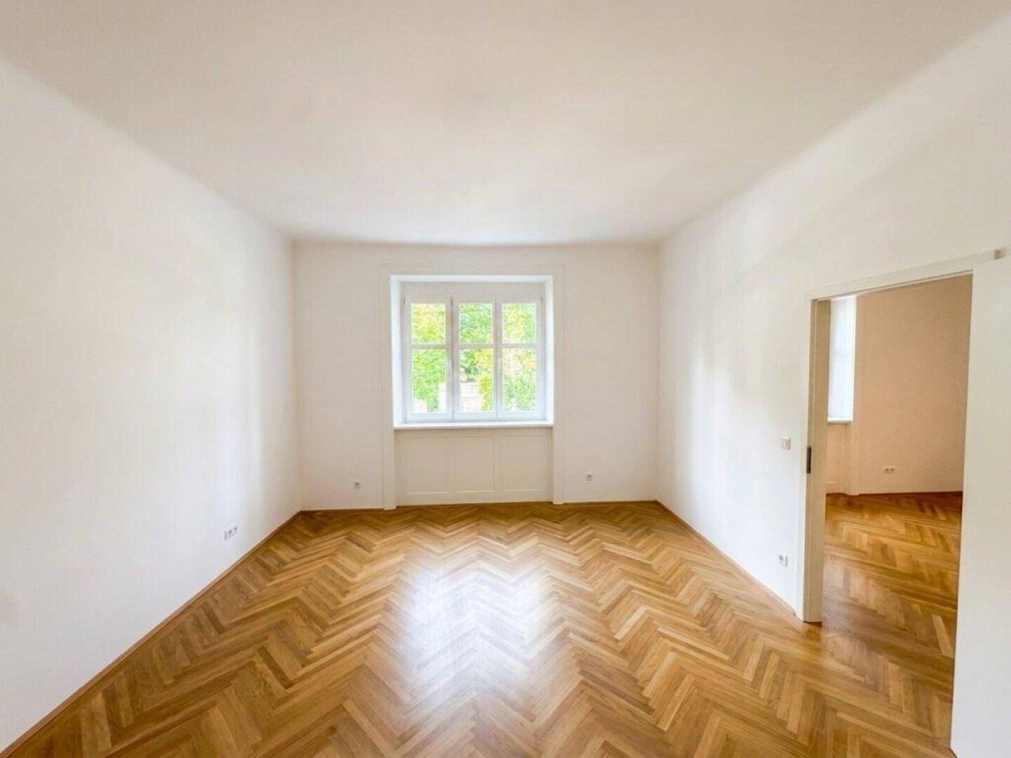 Ruhiges Zimmer mit Fischgrätparkett und großem Fenster, ideal als Schlaf- oder Arbeitszimmer.