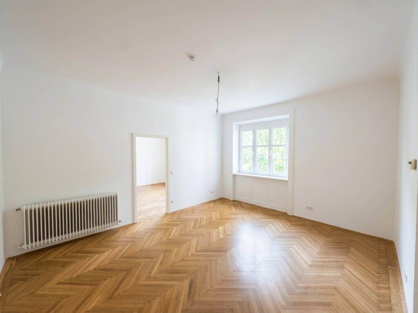 Helles Schlafzimmer mit Fischgrätparkett, hohen Decken und Blick ins Grüne.
