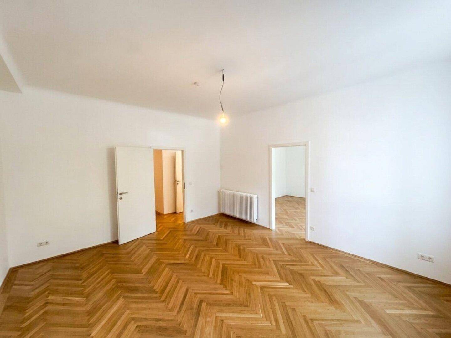Geräumiger Raum mit Fischgrätparkett und Zugang zu weiteren Zimmern, ideal für flexible Nutzung.