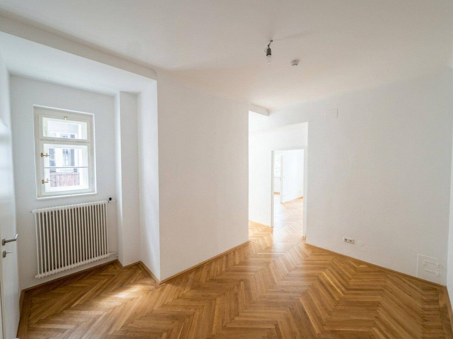 Heller Raum mit Fischgrätparkett und Fenster, der als Durchgangszimmer dienen könnte.