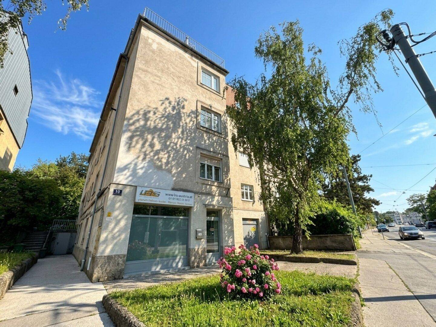 Mehrfamilienhaus mit klassischer Fassade und Geschäften im Erdgeschoss an einer Straße.