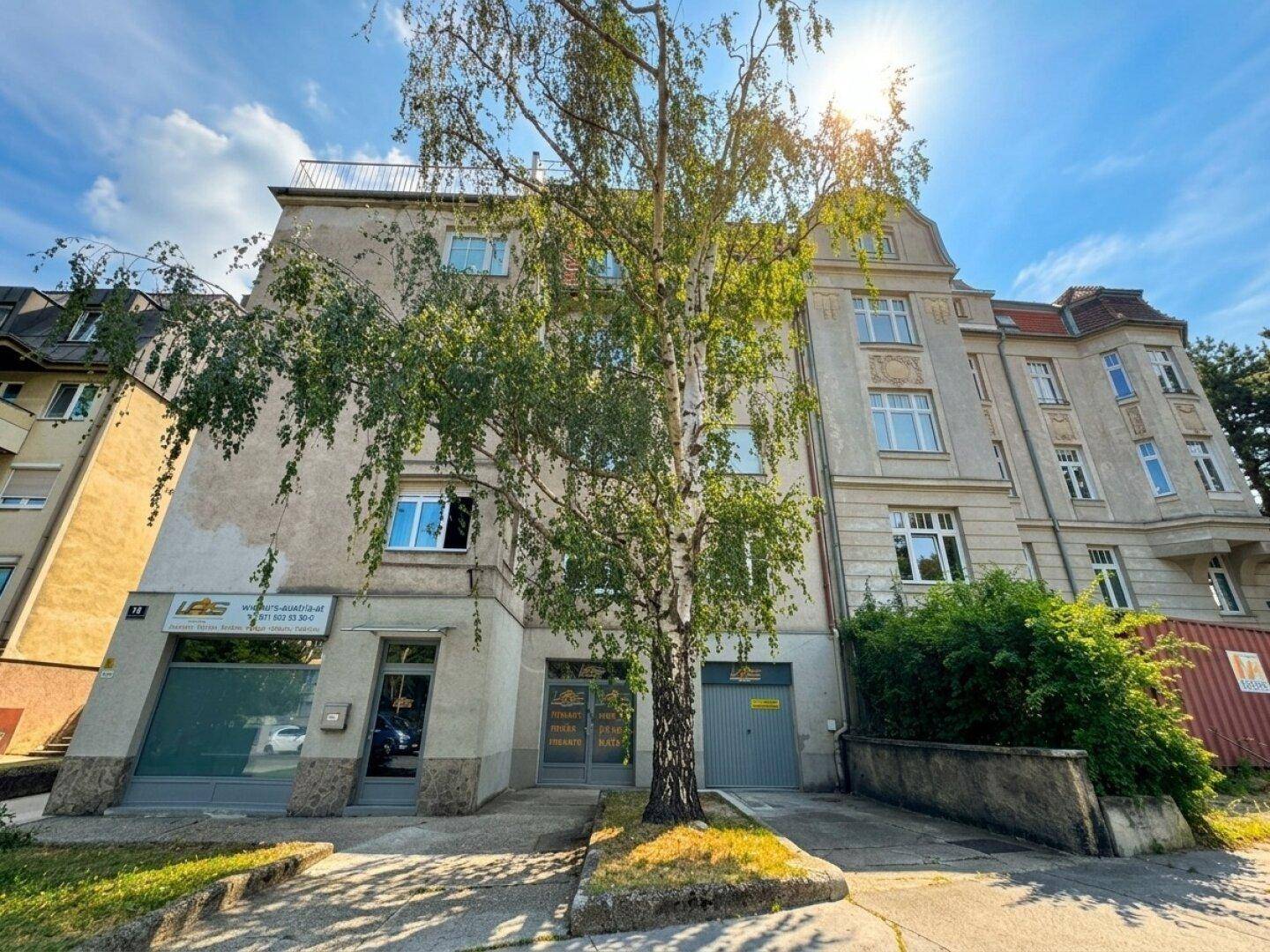 Historisches Gebäude mit mehreren Etagen, Bäumen und Geschäften im Erdgeschoss.