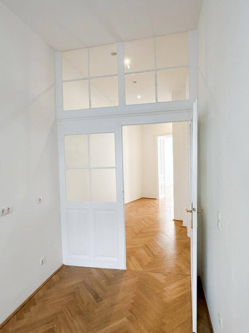 Geräumiger Küchenbereich mit Fischgrätparkett und hohen Türen mit Oberlichtfenstern.