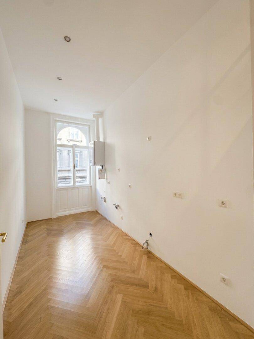 Langer, heller Raum mit Fischgrätparkett, vorbereitet für eine moderne Küche.