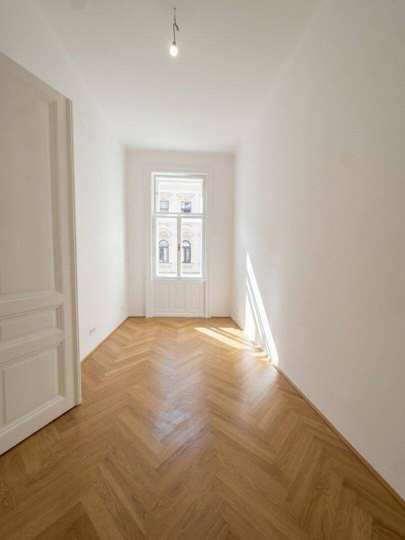 Langes, helles Zimmer mit Fischgrätparkett und einem hohen Fenster, ideal für ein Schlafzimmer.