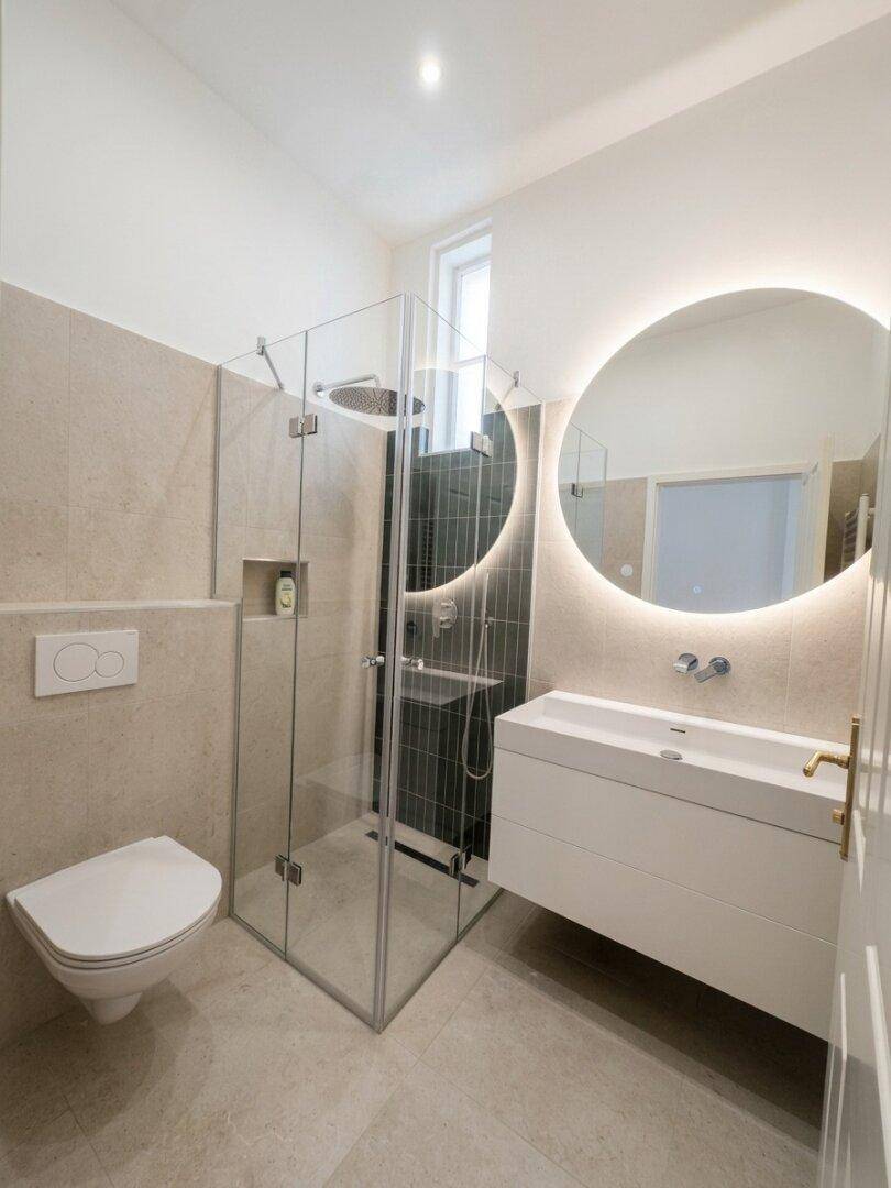 Modernes Badezimmer mit begehbarer Dusche, Wand-WC und beleuchtetem Spiegel.