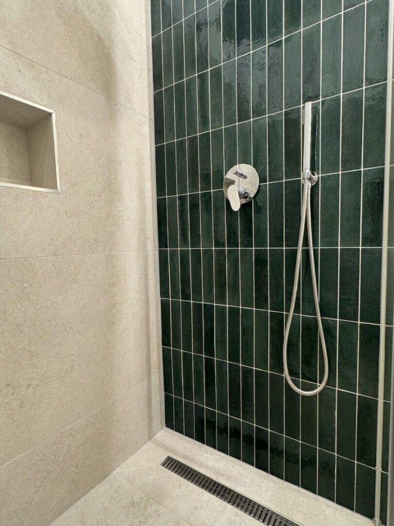 Detailansicht einer modernen begehbaren Dusche mit dunkelgrünen Fliesen und Regenbrause.