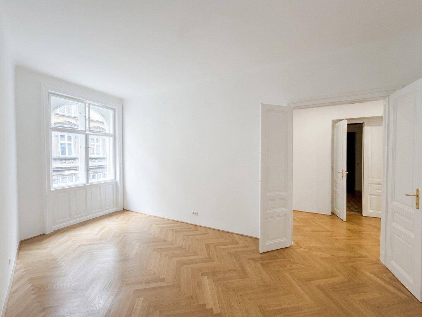 Großes, helles Zimmer mit Fischgrätparkett und Blick auf die gegenüberliegenden Gebäude.