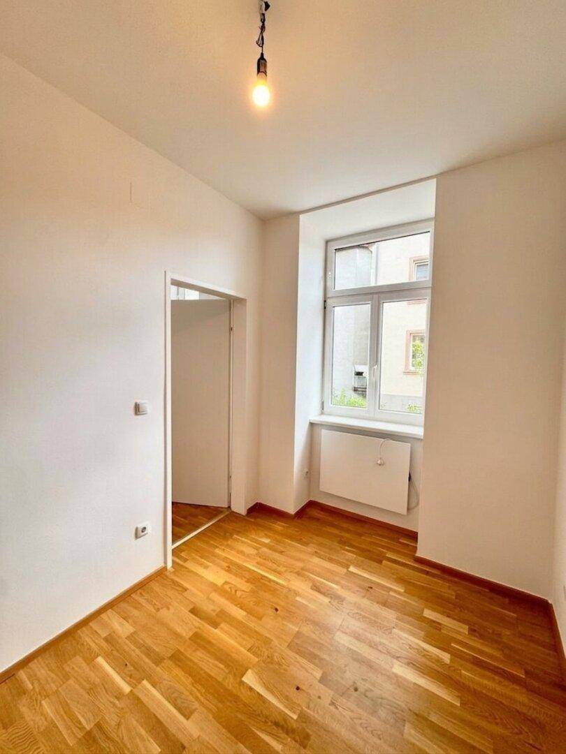 Helles Zimmer mit Parkettboden und einem Fenster mit Blick nach draußen.