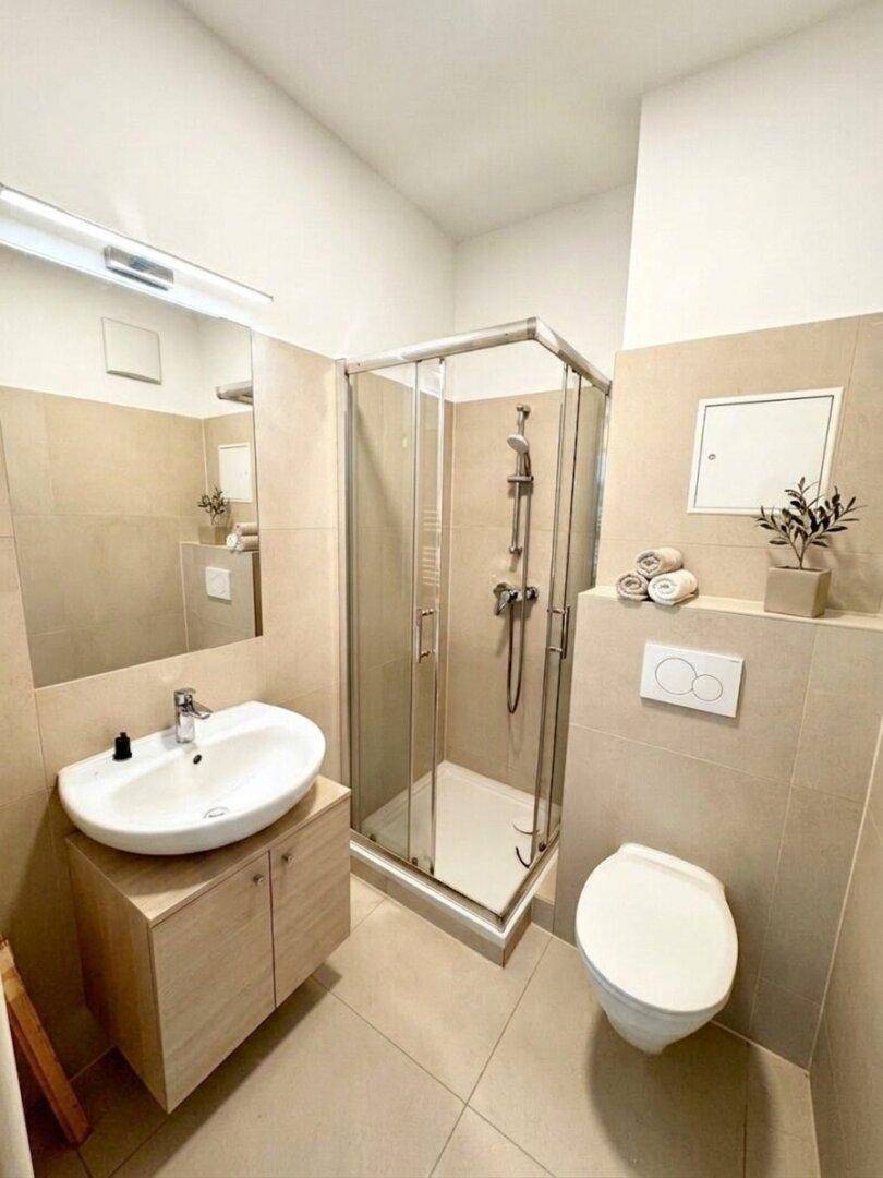 Gefliestes Badezimmer mit Duschkabine, Waschtischunterschrank und WC.