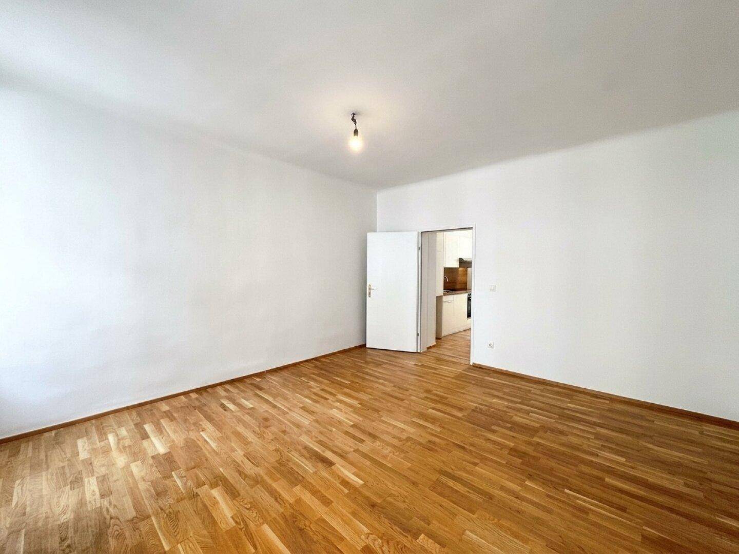 Helles Zimmer mit Parkettboden und offenem Zugang zu einem weiteren Raum.
