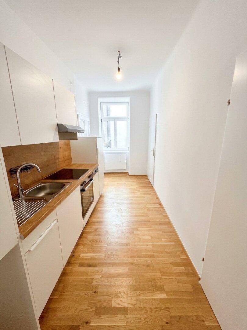 Lange, helle Küche mit Einbauschränken, Holzarbeitsplatte und Fenster für Tageslicht.